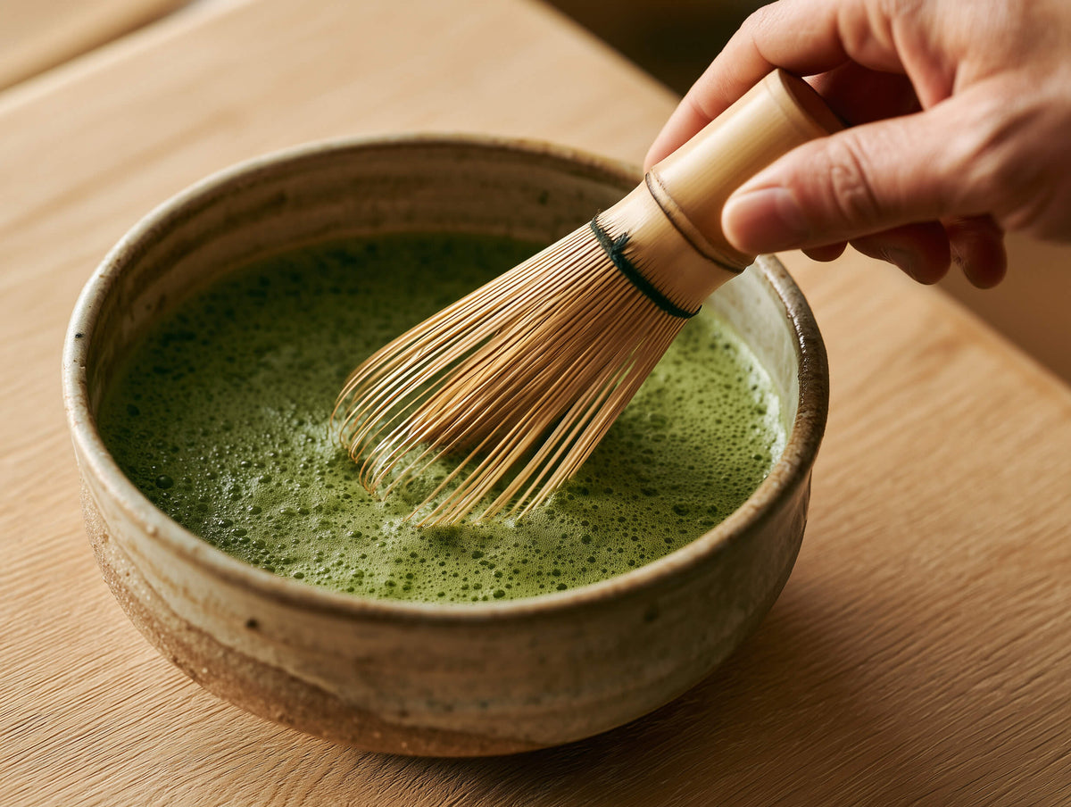 Matcha wird mit einem Bambus-Chasen in einer grünen Keramikschale aufgeschlagen
